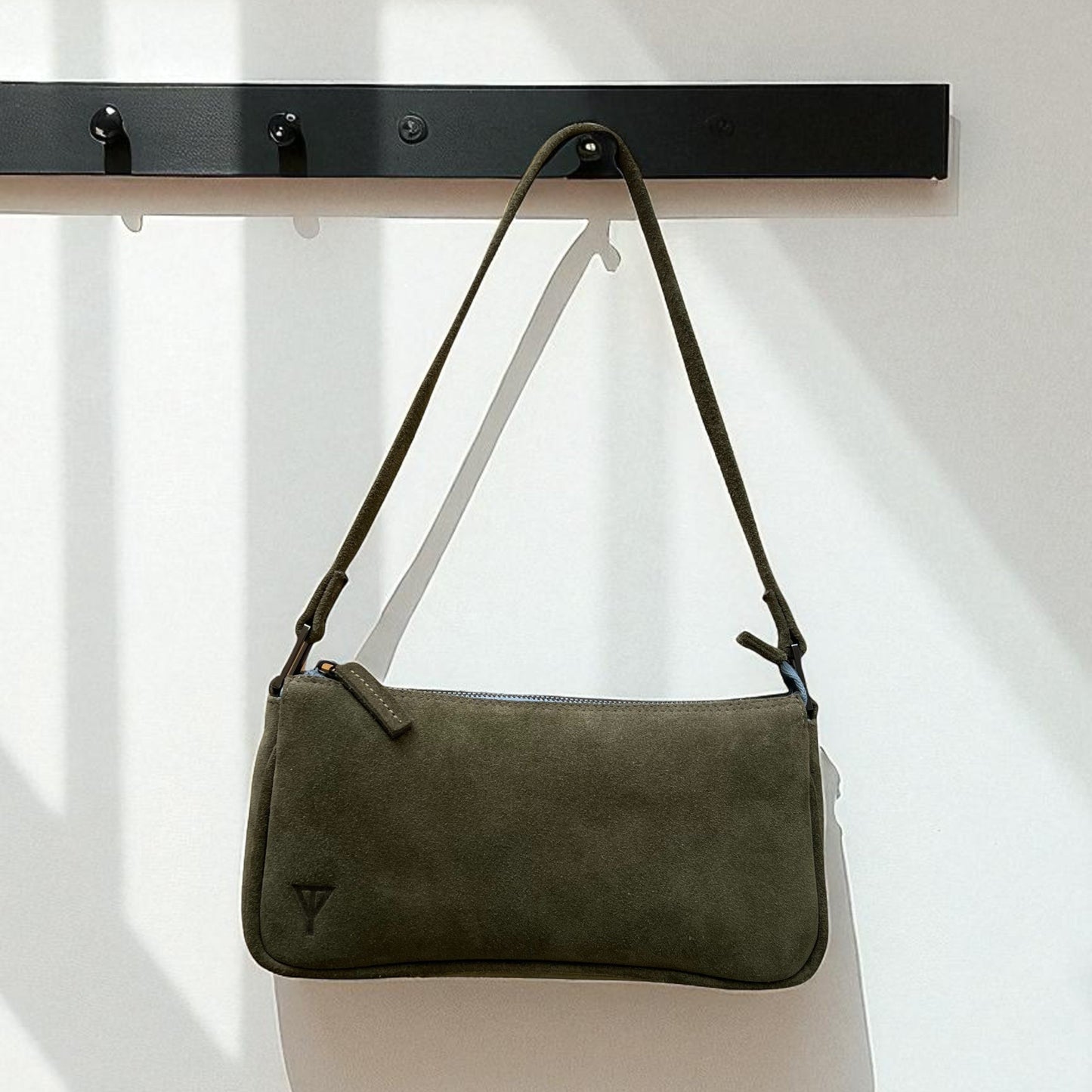 Green handbag hanging on a black rack against a white background