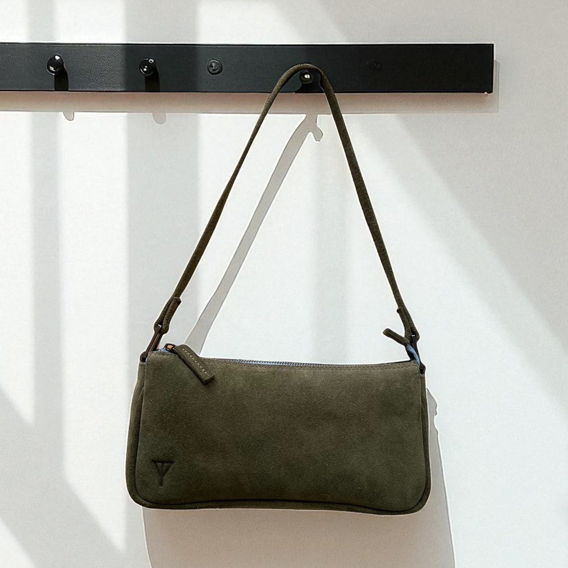 Green handbag hanging on a black rack against a white background
