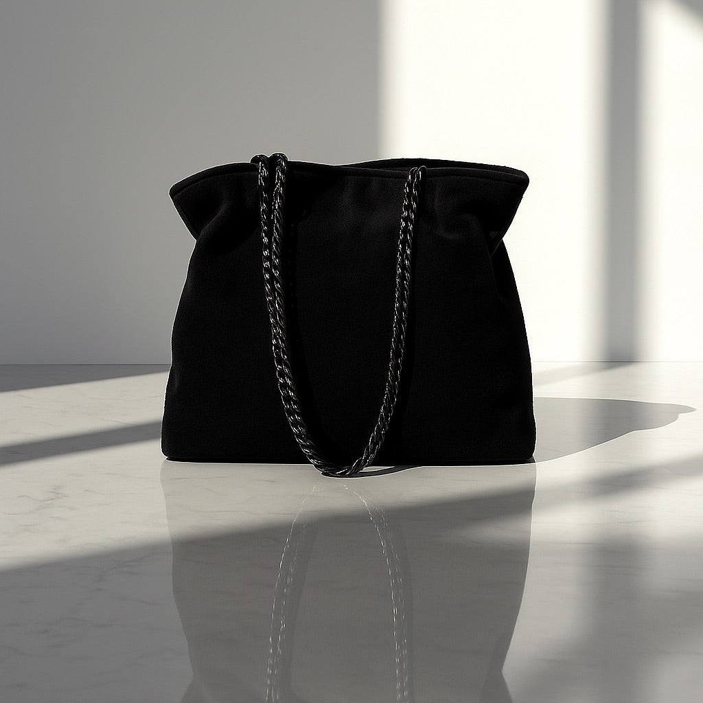 Black handbag with a chain detail on a reflective surface with light and shadow play.