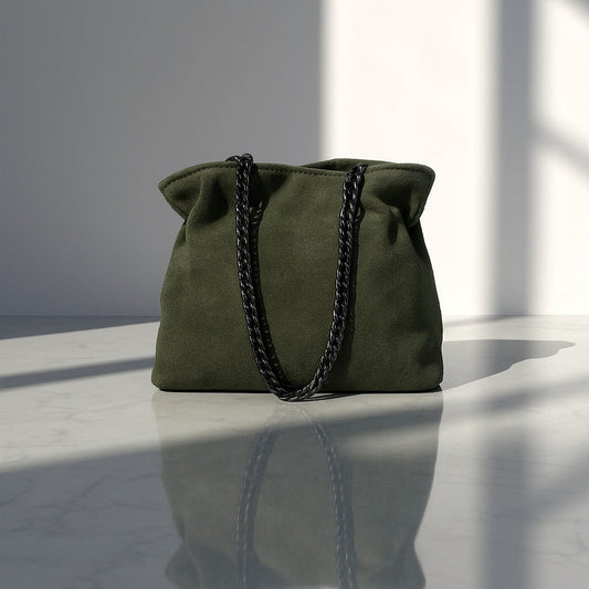 Green handbag with a chain detail on a reflective surface with light and shadow patterns.