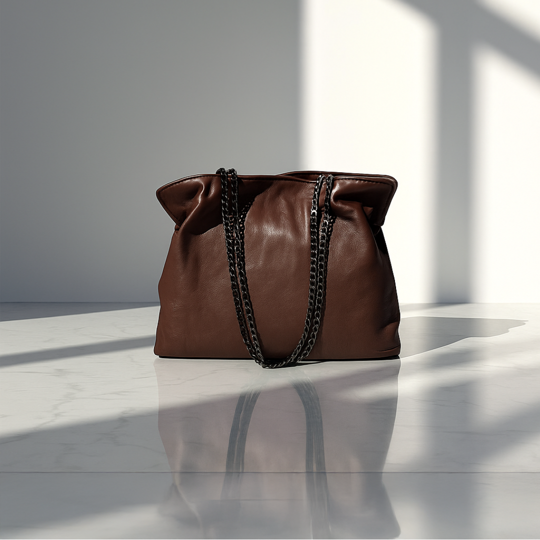 Chocolate Brown small leather handbag with black chain details on a white surface with light casting shadows.