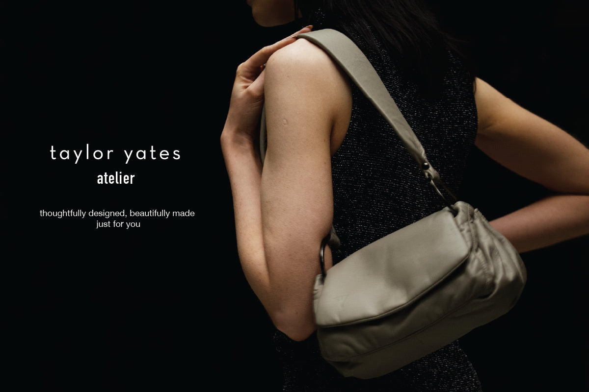 Person holding a porcini colour Norma shoulder bag with 'taylor yates atelier' branding on a black background