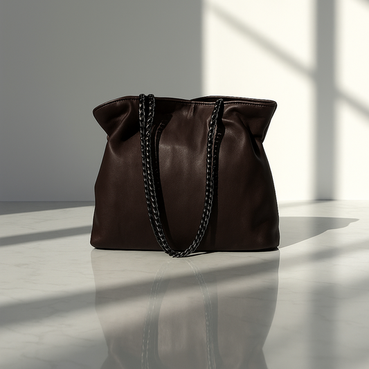 Dark Espresso Brown small leather handbag with black chain details on a white surface with light casting shadows.