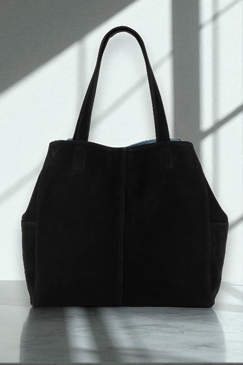 Black suede tote bag on a reflective surface with light casting shadows