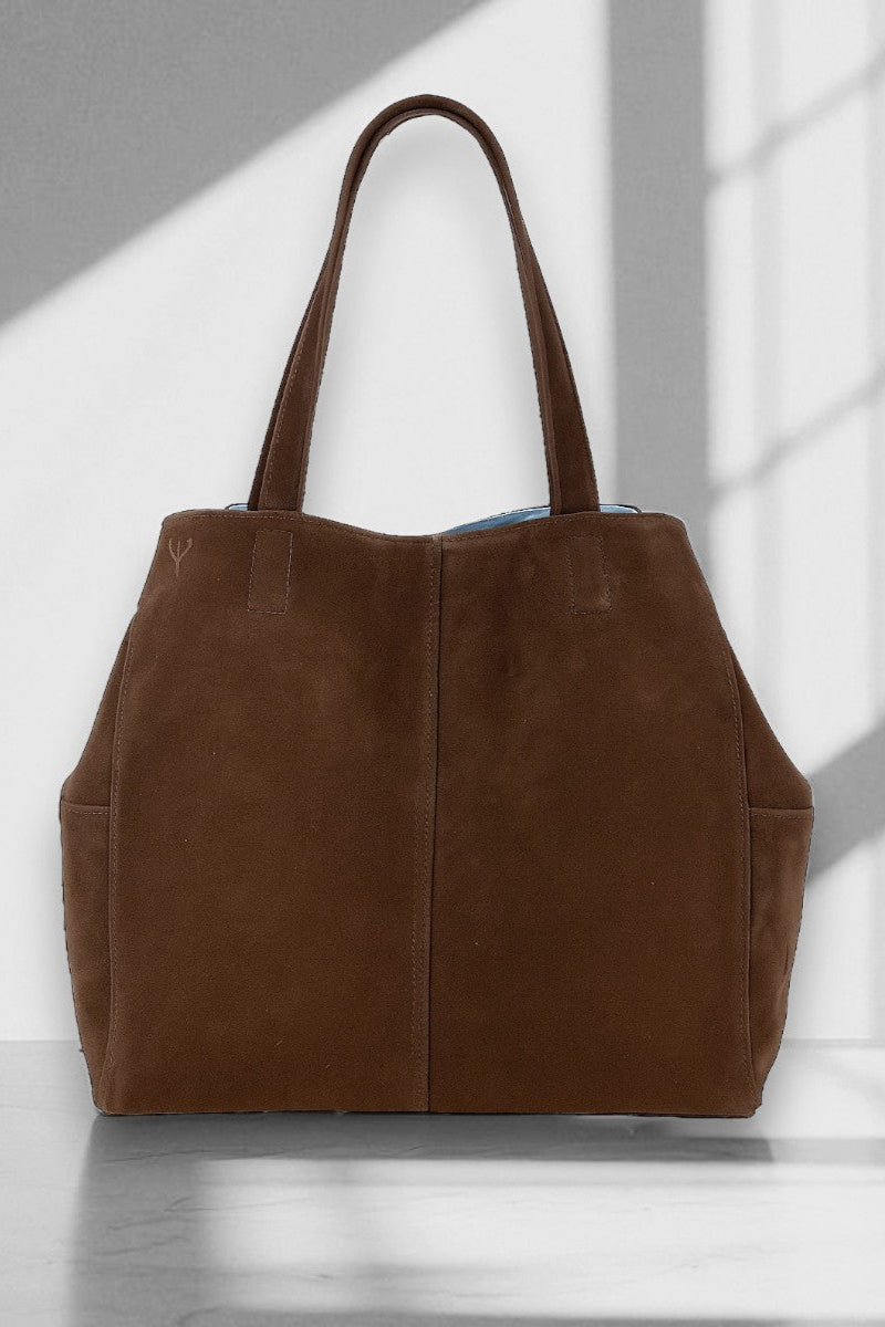 Brown suede tote bag on a white surface with a gray background