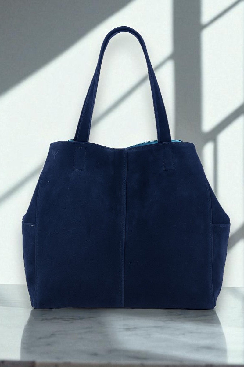 Navy blue suede tote bag on a marble surface with light filtering through a window.