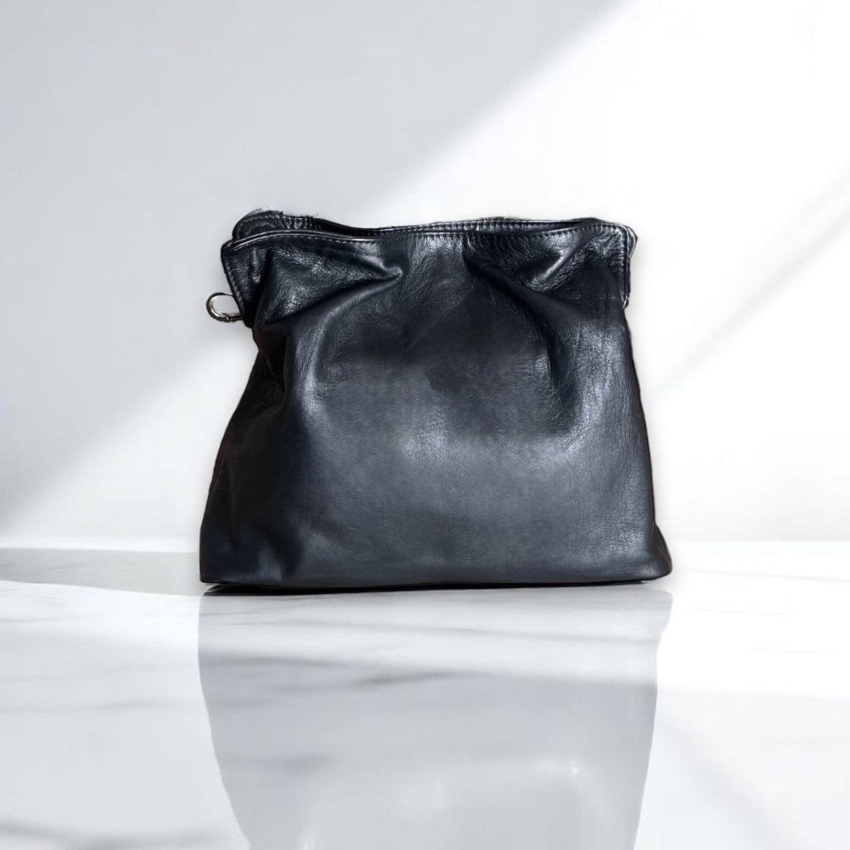 Soft leather clutch bag in Black Leather by Taylor Yates – front view on a white marble surface